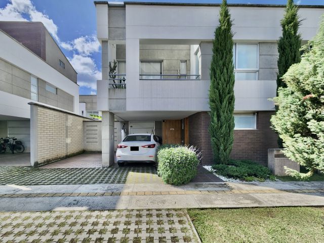 This stunning white house features two parking spaces (one covered and one uncovered) and a charming front garden with a pine tree. Perfect for those looking for a serene and inviting home in a gated community.